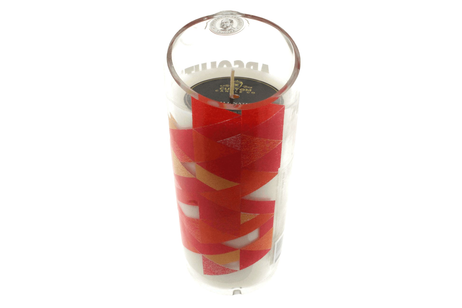 The Absolut Red Ruby Recycled Vodka Candle features a white, hand-poured soy candle in a cylindrical glass holder, adorned with geometric red, orange, and gold accents.