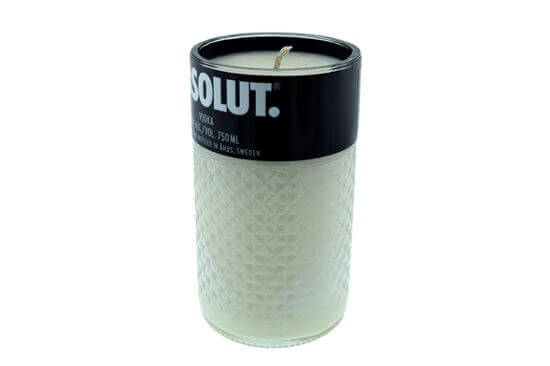 A white, hand-poured soy candle in a textured glass container made from recycled Absolut vodka bottles, featuring a black label with "SOLUT" at the top. All-natural ingredients ensure a clean burn.