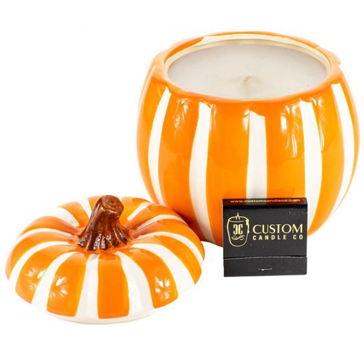 The Ceramic Large Orange/White Line Pumpkin Candle features a pumpkin-shaped ceramic holder with orange and white stripes, its lid off to reveal a white candle inside. A Custom Candle Co. label is displayed in front of the holder.