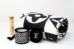 A rolled cotton throw with a black and white pattern, a small candle with a black LV lid, and a glass vial of matches are shown on a white background—ideal accents for Custom Design Baskets or thoughtful gift sets.