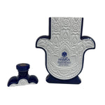 A Casa de Hamsa Blanco bottle, white and blue and shaped like a Hamsa hand, stands with its matching cap on a white background.