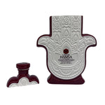 A ceramic bottle shaped like a Hamsa hand, labeled "Casa de Hamsa Reposado," stands next to its matching cap—a unique piece perfect for displaying a cruelty-free or recycled soy candle.