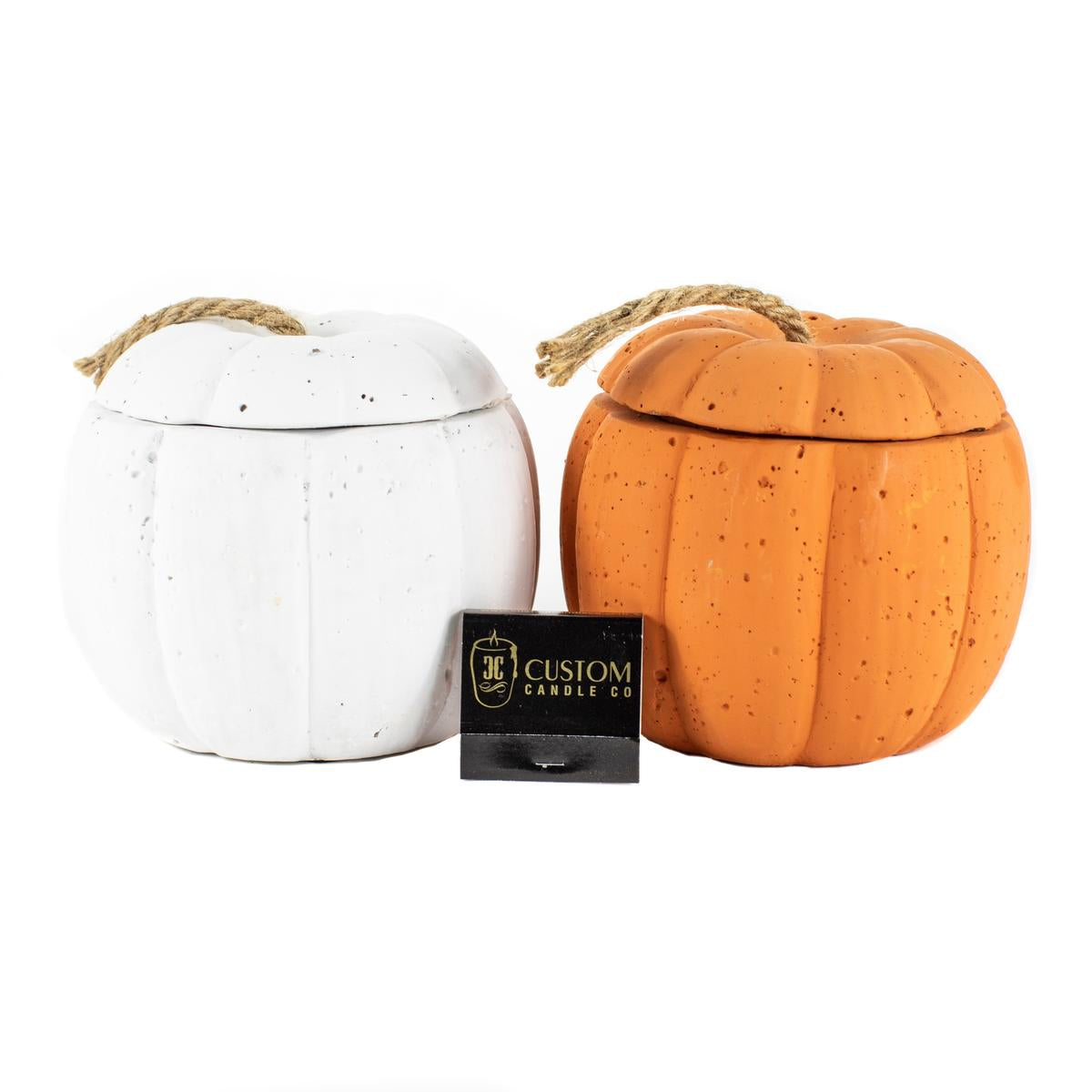 The Orange Cement Candle and a white pumpkin-shaped candle, both with rope-handled lids, are shown beside a stylish black "Custom Candle Co" box.