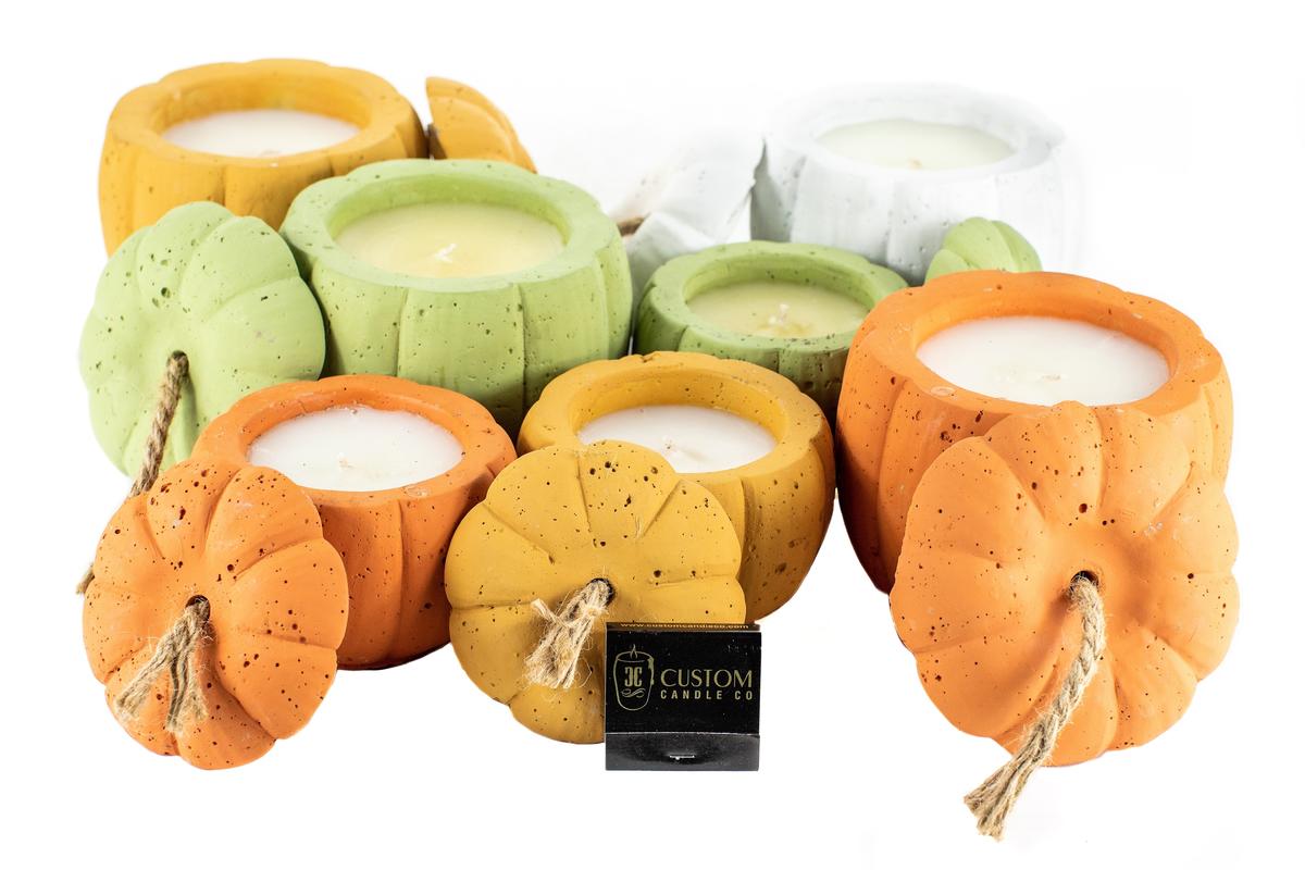 The Orange Cement Candle, featuring a pumpkin shape with a rope stem, is shown grouped with custom candle designs in orange, green, and white on a white background.