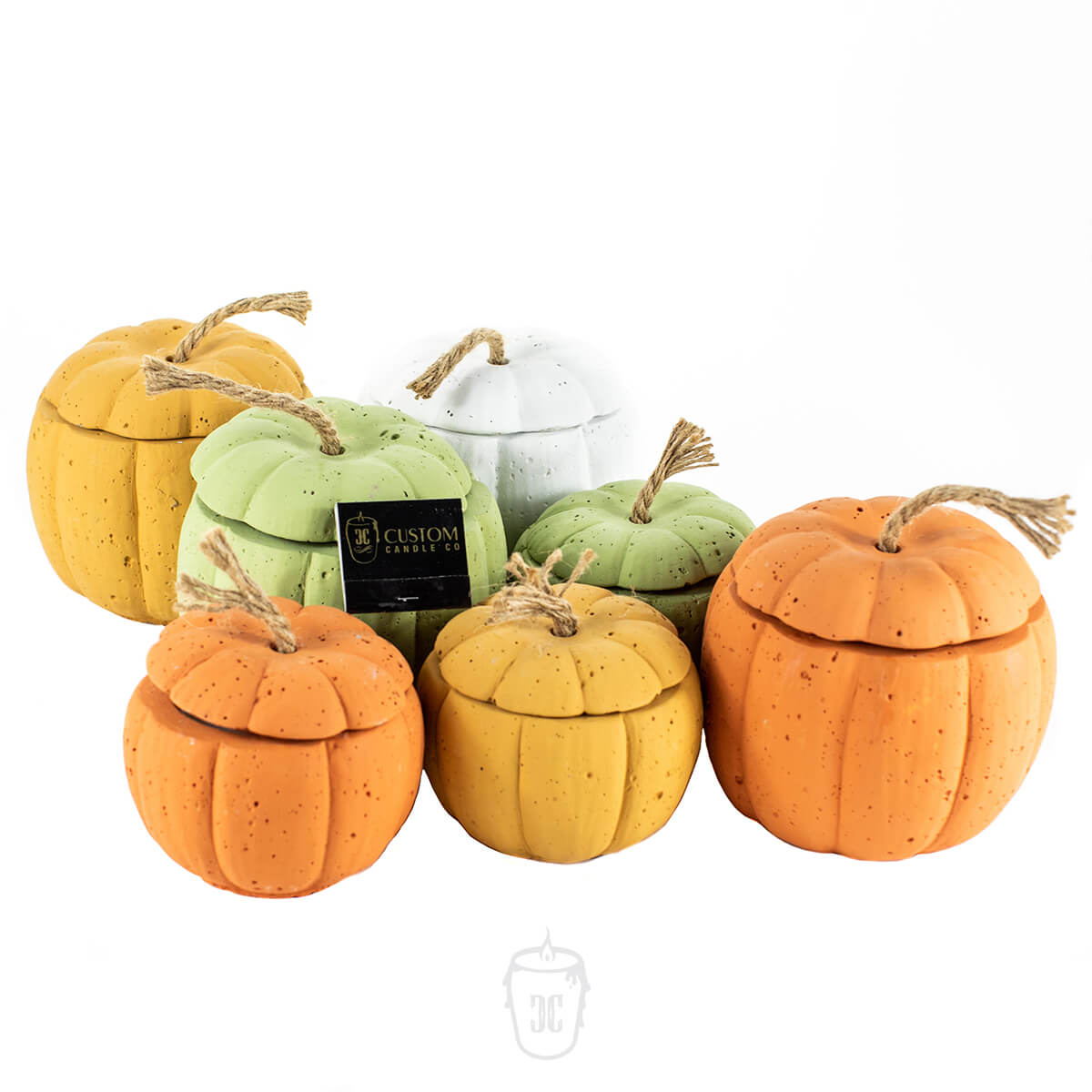 Assorted ceramic pumpkin jars in orange, green, and white with rope stems are grouped beside a Yellow Cement Candle on a white background.
