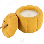 A Yellow Cement Candle in a pumpkin-shaped yellow container with the lid removed and set beside it.