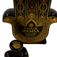 The Casa de Hamsa Añejo Tequila Candle features a black and gold hamsa-shaped tequila bottle with a matching stopper, paired with a recycled hand-poured natural soy candle.