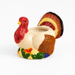 The Turkey Candle, a ceramic candle with colorful tail feathers and a hollow center, brings festive charm to your Thanksgiving décor, shown against a white background.