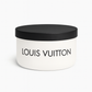 A white round container with a black lid holds the Luxury White Two-Wick Candle – Inspired by Iconic Designer Style, featuring "Louis Vuitton" in bold black letters on the front and made with premium soy wax.