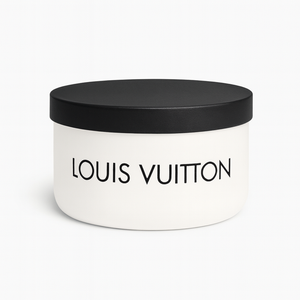 A white round container with a black lid holds the Luxury White Two-Wick Candle – Inspired by Iconic Designer Style, featuring "Louis Vuitton" in bold black letters on the front and made with premium soy wax.