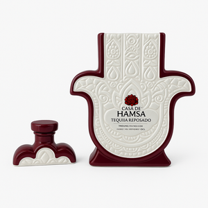 A Casa de Hamsa Reposado bottle, recycled into a natural soy candle with an embossed hamsa design, sits next to its matching cap on a white background.