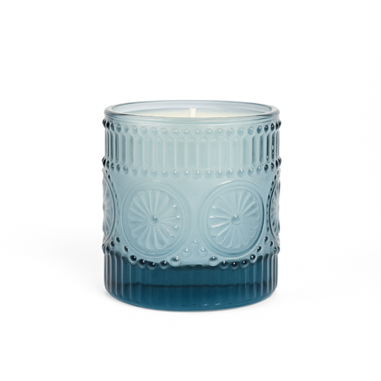 The Blue Embossed Glass Candle features a decorative natural wax candle in a glass holder with raised circular and dot patterns.