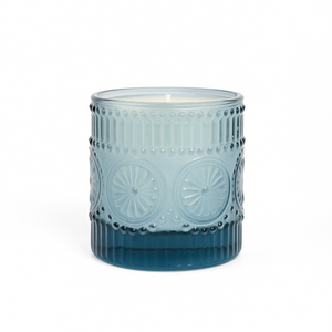 The Blue Embossed Glass Candle features a decorative natural wax candle in a glass holder with raised circular and dot patterns.