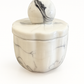 The Marble Luxe Candle features a round, white marble-patterned ceramic container with a matching lid and spherical handle, bringing luxury and elegance to any space. Set against a plain white background.