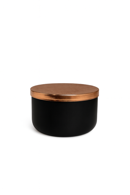 The Designer Noir Candle features a round black container with a metallic copper lid, adding sophistication to any space. Shown here against a plain white background.