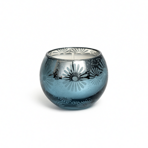 The Metallic Snowburst Candle features a blue glass holder with a floral metallic interior and round shape, making it perfect for holiday decor. Displayed on a white background for an elegant touch.
