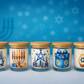 Assorted Hanukkah Candle set: five glass jars with wooden lids, each adorned with Hanukkah-themed illustrations like menorahs, candles, gift boxes, and a dreidel—perfect festive holiday gifts against a blue background.