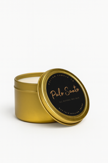 A gold-toned tin from the Palo Santo Box Set, with a partially open lid, displays a white candle inside.