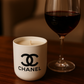 A Designer Ceramic Candle sits on a wooden surface next to a glass of red wine.