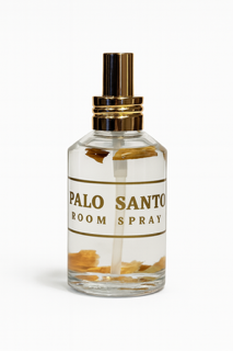 Clear glass bottle labeled "Palo Santo Box Set" with gold details and visible wood pieces inside, set against a white background.