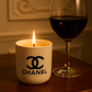 A lit Designer Ceramic Candle and a glass of red wine rest on a wooden surface, set against an ornate wall background.