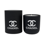 The Designer Ceramic Candle is a black soy candle with a white logo, shown beside its matching cylindrical reusable jar, displayed against a white background.