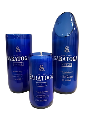 Three blue Saratoga Still Natural Spring Water bottles—two upcycled into drinking glasses and one made into an eco-friendly candle—are displayed side by side against a white background.