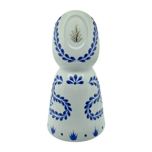 The Recycled Azul Tequila Curve Cut Candle features a white ceramic bottle with blue floral designs and a silver agave emblem, hand-poured with soy wax and photographed against a plain white background.