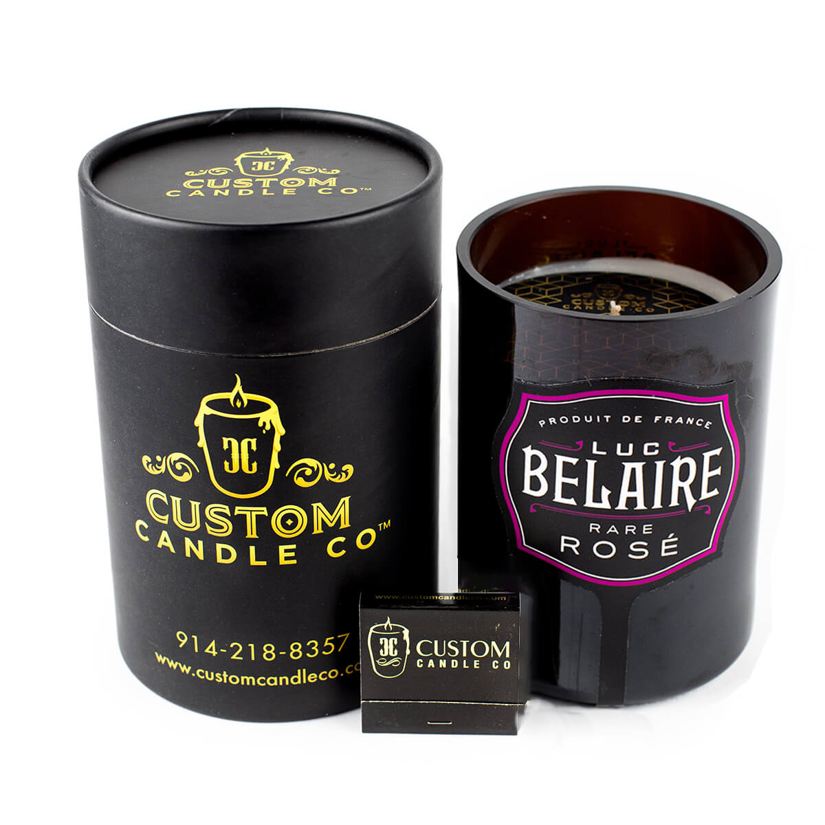 A black cylindrical Custom Candle container sits beside an open Recycled Champagne Candle – Luc Belaire Rare Rose, with a small matchbox in front.