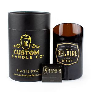 A black cylindrical custom candle container, a Recycled Champagne Candle – Luc Belaire Rare Brut, and a Custom Candle Co. matchbox are displayed against a white background.