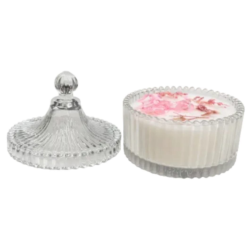 The Pressed Flower Candle - Crystal Glass Jar features a clear ribbed crystal glass jar with a matching lid, holding a soy candle adorned with small pink flowers—perfect for adding beauty to any space.