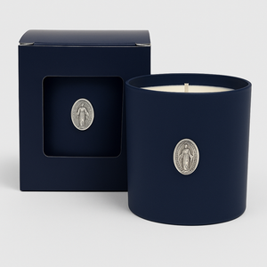 The Boxed Blessed Mother Candle, in dark blue coconut-apricot wax with a silver religious medallion, comes in a matching box featuring a window that displays the same medallion.