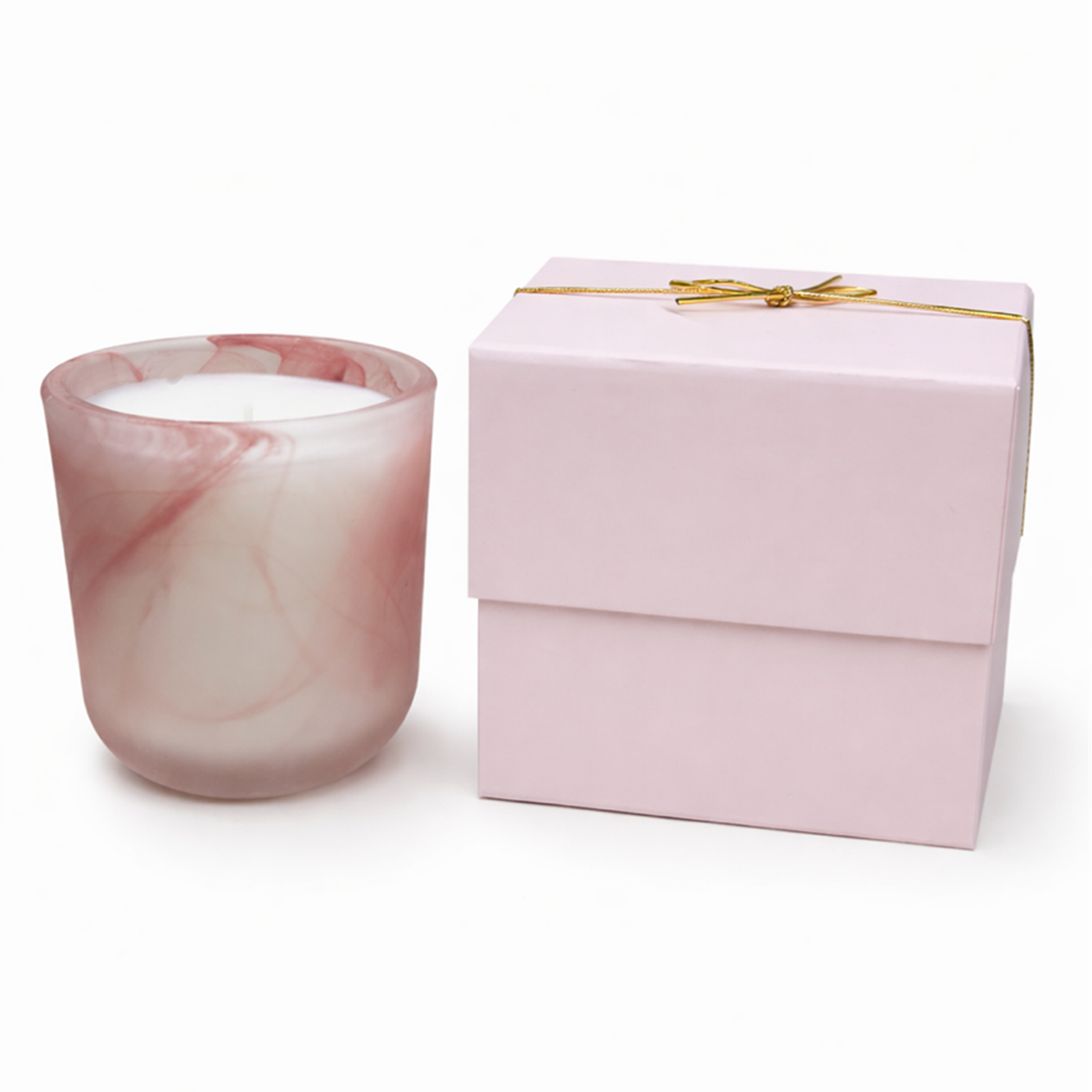 The Frosted Pink Sonoma Candle with a pink and white marbled rose scent in a glass holder sits next to a closed pink gift box tied with a thin gold ribbon.
