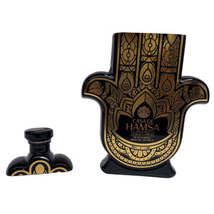 A black and gold Casa de Hamsa Añejo tequila bottle, shaped like a Hamsa hand with an intricate design and matching cap, is shown—ideal as a custom candle or Tequila Candle for distinctive decor.