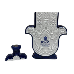 A Casa de Hamsa Blanco bottle, white and blue and shaped like a Hamsa hand, stands with its matching cap on a white background.