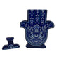 The Casa de Hamsa Blanco is a ceramic container shaped like a Hamsa hand, featuring a blue and white decorative pattern, shown with its matching lid beside it on a white surface.