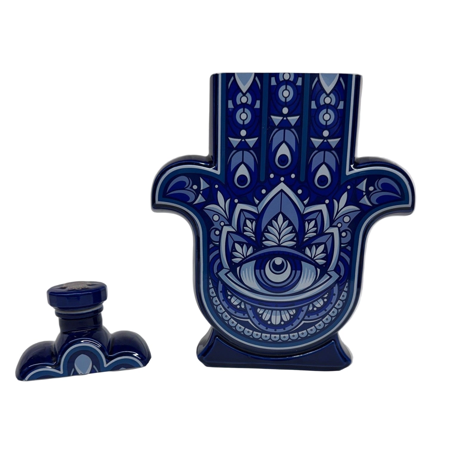 The Casa de Hamsa Blanco is a ceramic container shaped like a Hamsa hand, featuring a blue and white decorative pattern, shown with its matching lid beside it on a white surface.