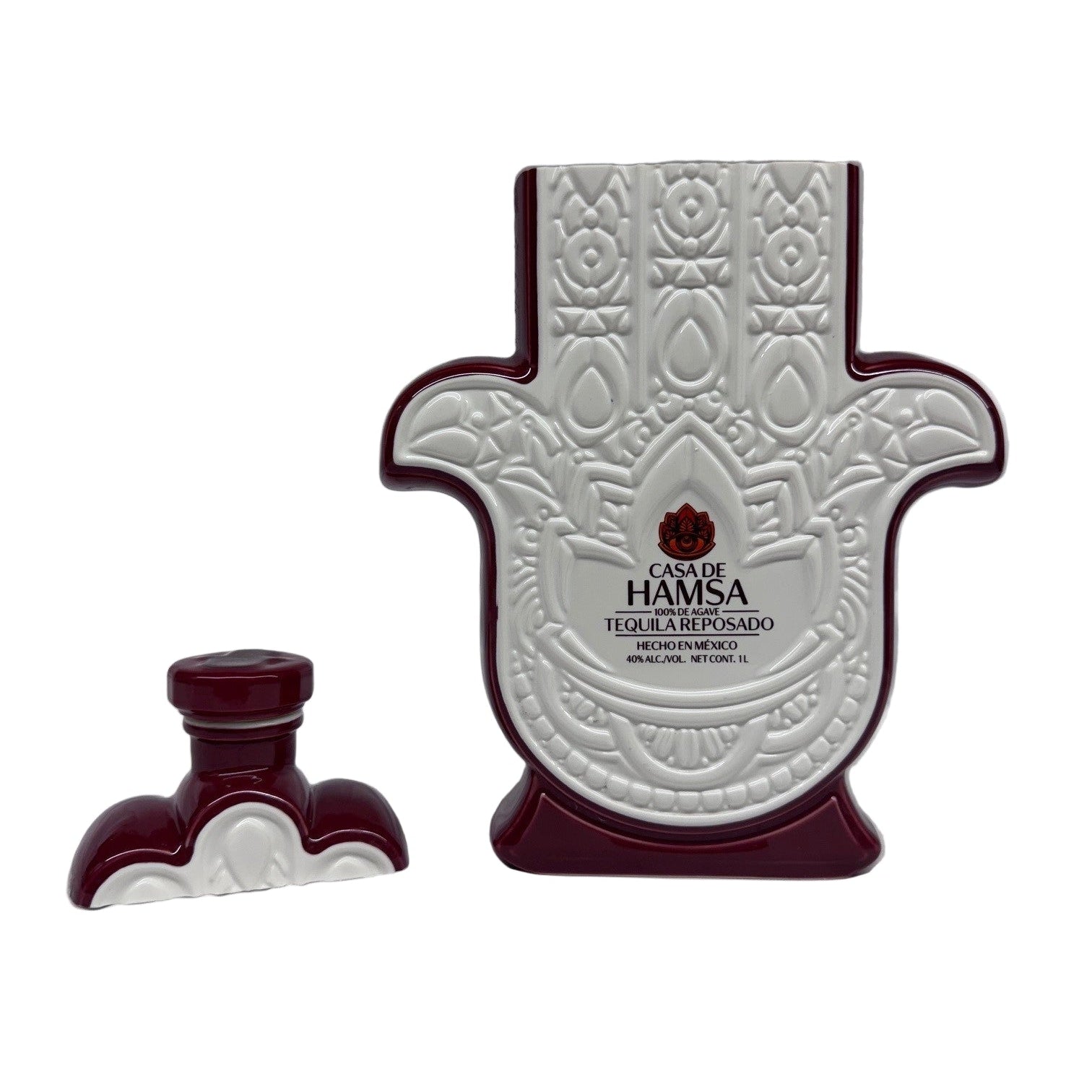 A ceramic bottle shaped like a Hamsa hand, labeled "Casa de Hamsa Reposado," stands next to its matching cap—a unique piece perfect for displaying a cruelty-free or recycled soy candle.