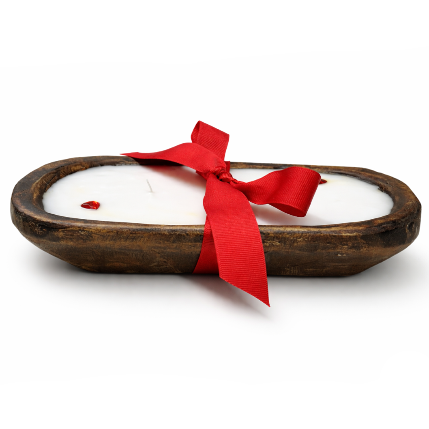 The Red Ribbon - Dough Bowl Candle is a hand-poured soy candle in a rustic oval wooden holder, decorated with a red ribbon bow and red accents, shown on a white background.