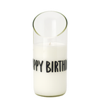 The "Happy Birthday" Recycled Curve Cut Candle, made from natural wax, sits in a clear glass holder with "HAPPY BIRTHD" in black letters and features a slanted top edge.