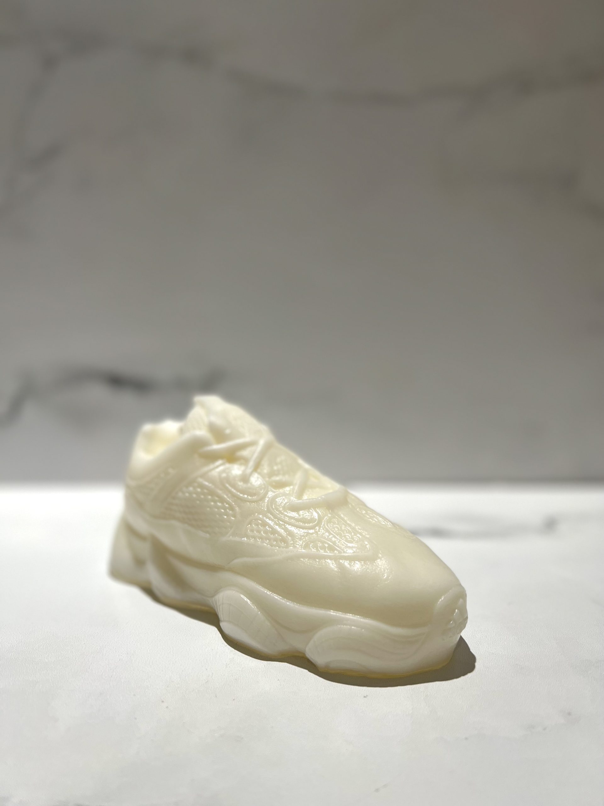 The Y500 – White Sneaker Candle – Small, hand-poured from a smooth white material and infused with black ice fragrance, rests on a flat surface against a plain background.