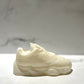 The Y500 – White Sneaker Candle – Small is a hand-poured candle shaped like a white sneaker, displayed on a light surface with a softly blurred background.