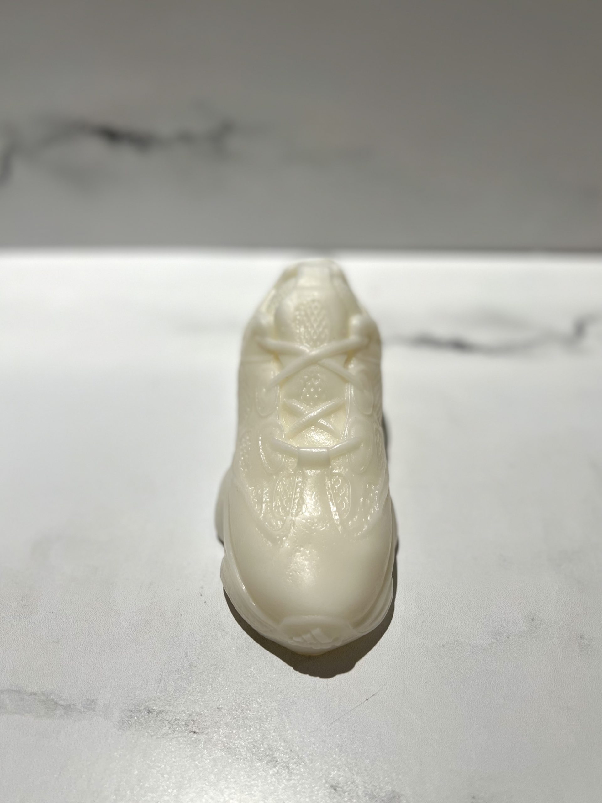 The Y500 – White Sneaker Candle – Small is a hand-poured, sneaker-shaped candle in white, displayed on a smooth light surface with a subtle marble-patterned background.