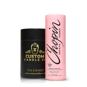 A Recycled Chopin Potato Vodka Candle from Custom Candle Co., made from a black upcycled bottle, sits beside a tall pink Chopin Potato Vodka special edition tube.