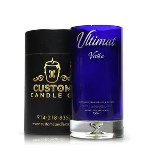 A Recycled Ultimat Vodka Candle in a blue bottle sits beside a black Custom Candle Co. container featuring gold text and logo.