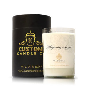 A white Recycled Whispering Angel Rose Wine Candle, crafted from upcycled materials, sits next to a black cylindrical box with gold Custom Candle Co. branding and contact information.