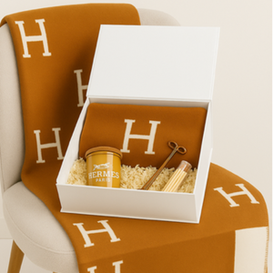 The Designer Orange Paris Gift Set features an orange Hermes blanket, a scented candle, wick trimmer, and matches in a white gift box on a cream chair with a matching Hermes throw—ideal for custom baskets.