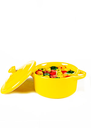 The Yellow Mini Cereal Crockpot Candle is shown with its lid partially open, displaying an assortment of colorful vegetables inside, all set against a white background.