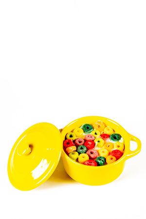 The Yellow Mini Cereal Crockpot Candle features colorful, round cereal pieces in milk inside a yellow pot with a matching lid, resembling a playful, fruity scented candle against a white background.