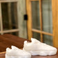 Two Y500 – White Sneaker Candle – Small, each meticulously hand poured, are displayed on a wooden surface before glass-paneled wooden doors.